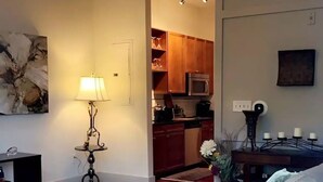 A living room with a sofa, a lamp, and a kitchen in the background. - Lovely Condo in the Very Heart of NoDA (Charlotte)