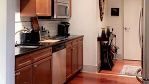 A modern kitchen with wooden cabinets, a microwave, and a coffee maker. There is a rug on the floor and a door in the background. - Lovely Condo in the Very Heart of NoDA (Charlotte)