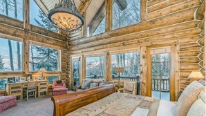 Ein Schlafzimmer in einer Blockhütte mit einem großen Bett, zahlreichen Fenstern und Blick auf den Wald.