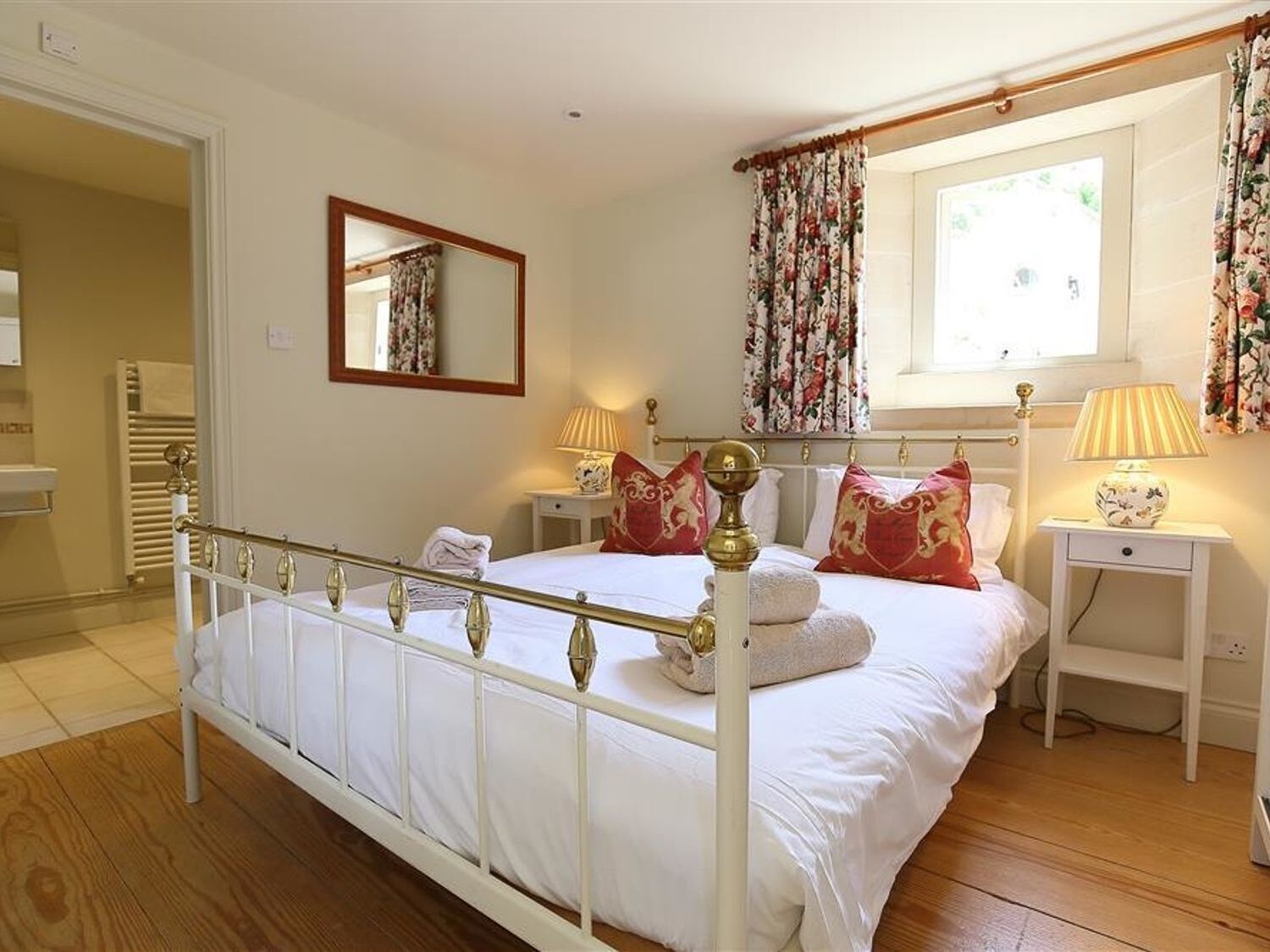 Une chambre à coucher bien rangée, avec un lit blanc, des rideaux à motifs floraux et une lampe de chevet.