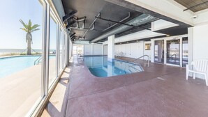 Une piscine intérieure offrant une vue dégagée sur l’océan, avec un sol en béton et un plafond laissant apparaître les tuyaux.