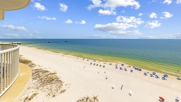 Une plage offrant une vue dégagée sur l’océan, une jetée visible au loin, ainsi que des parasols et des chaises de plage le long du rivage.