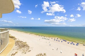 Ein Strand mit freiem Blick auf das Meer, ein Steg in der Ferne sowie Strandsonnenstühle und -schirme am Ufer.
