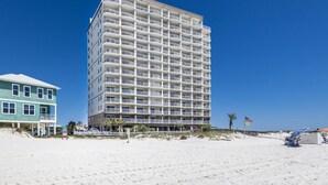 Un hôtel à plusieurs étages, doté de balcons, situé sur une plage où le ciel est dégagé.
