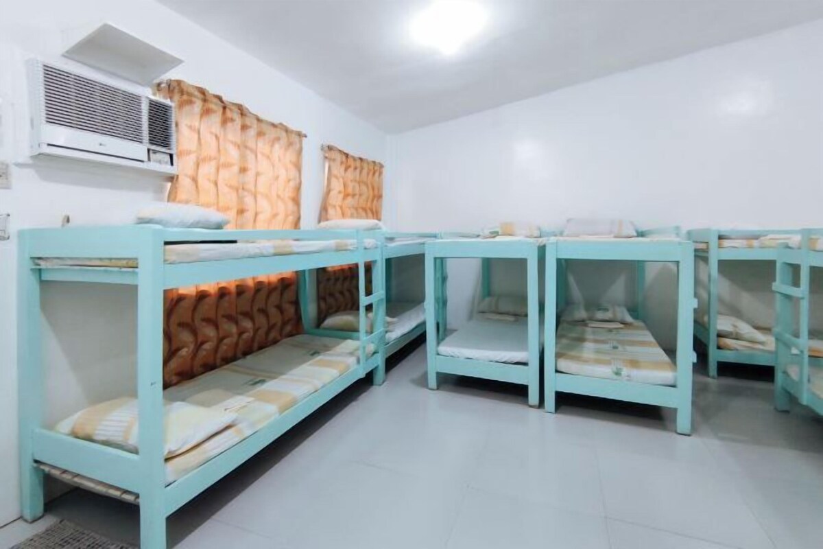 A dormitory room with bunk beds, a window with curtains, and an air conditioning unit.
