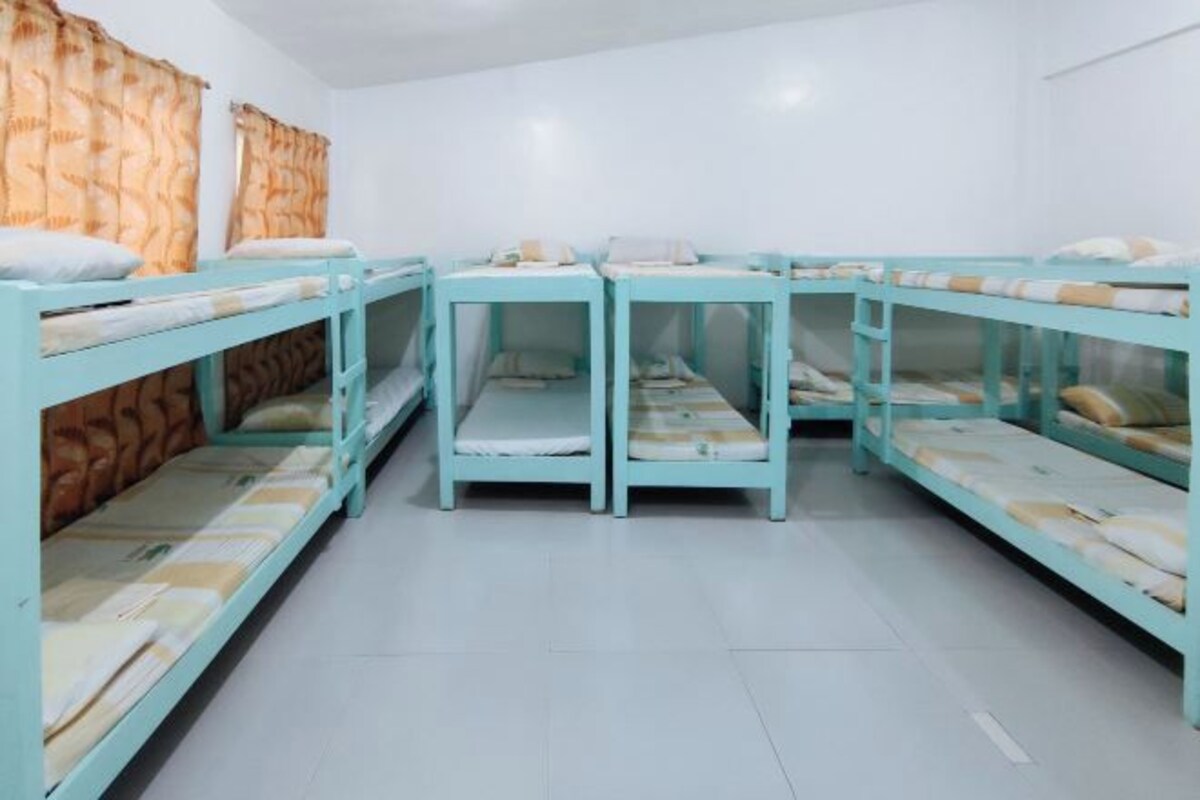 A dormitory room with bunk beds arranged in a U-shape, white walls, and a tiled floor.