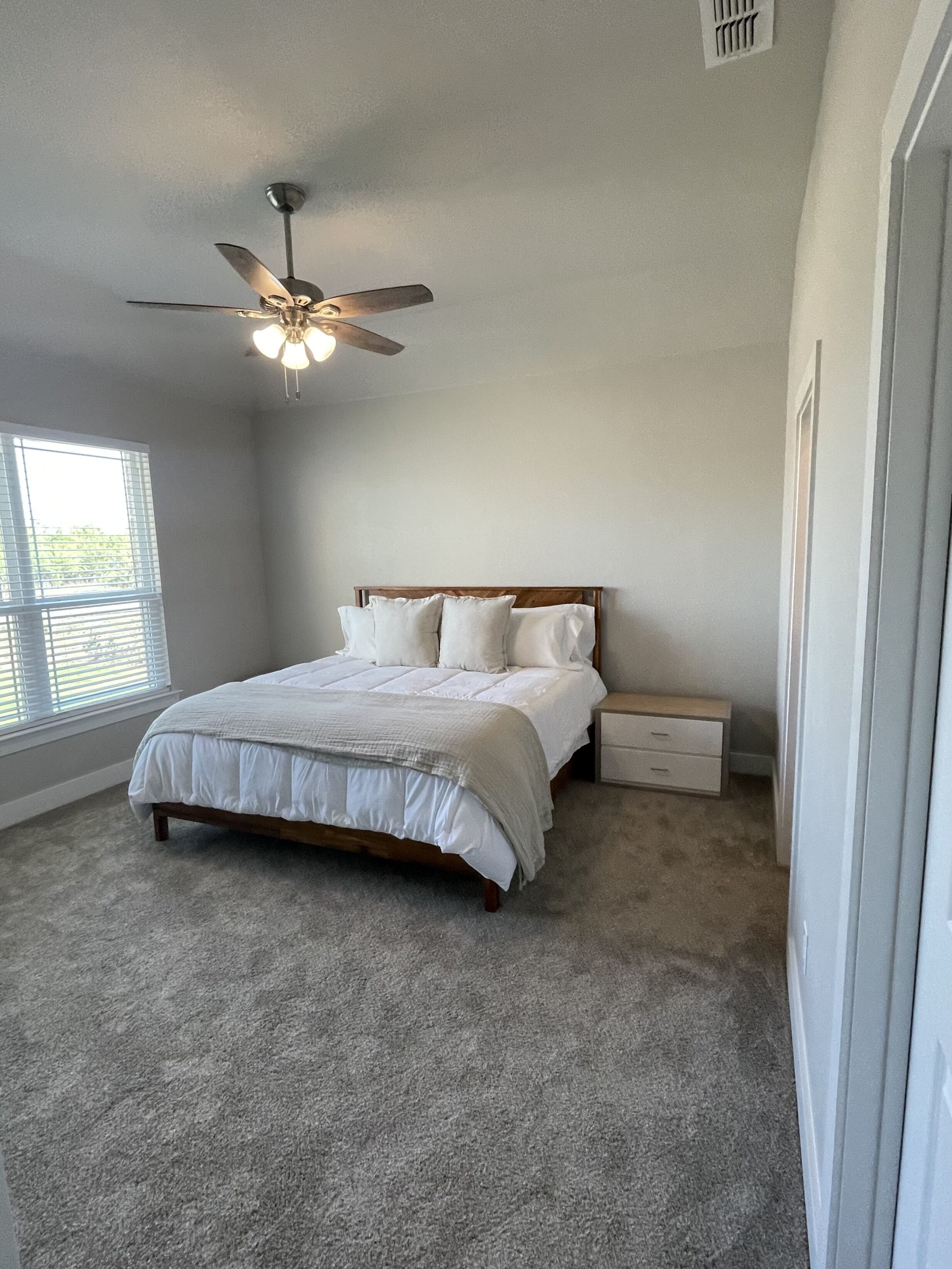A bedroom with a bed, a nightstand, a ceiling fan, and a window with blinds.