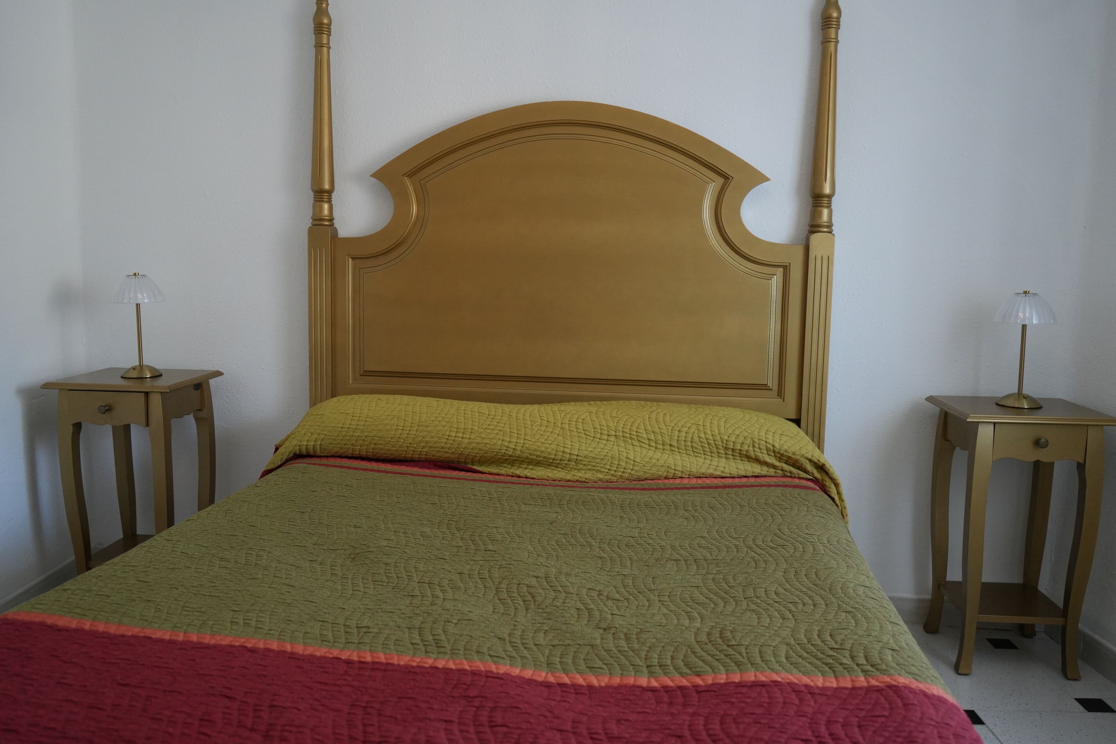 Een kamer met een hemelbed, twee nachtkastjes en een effen muur.
