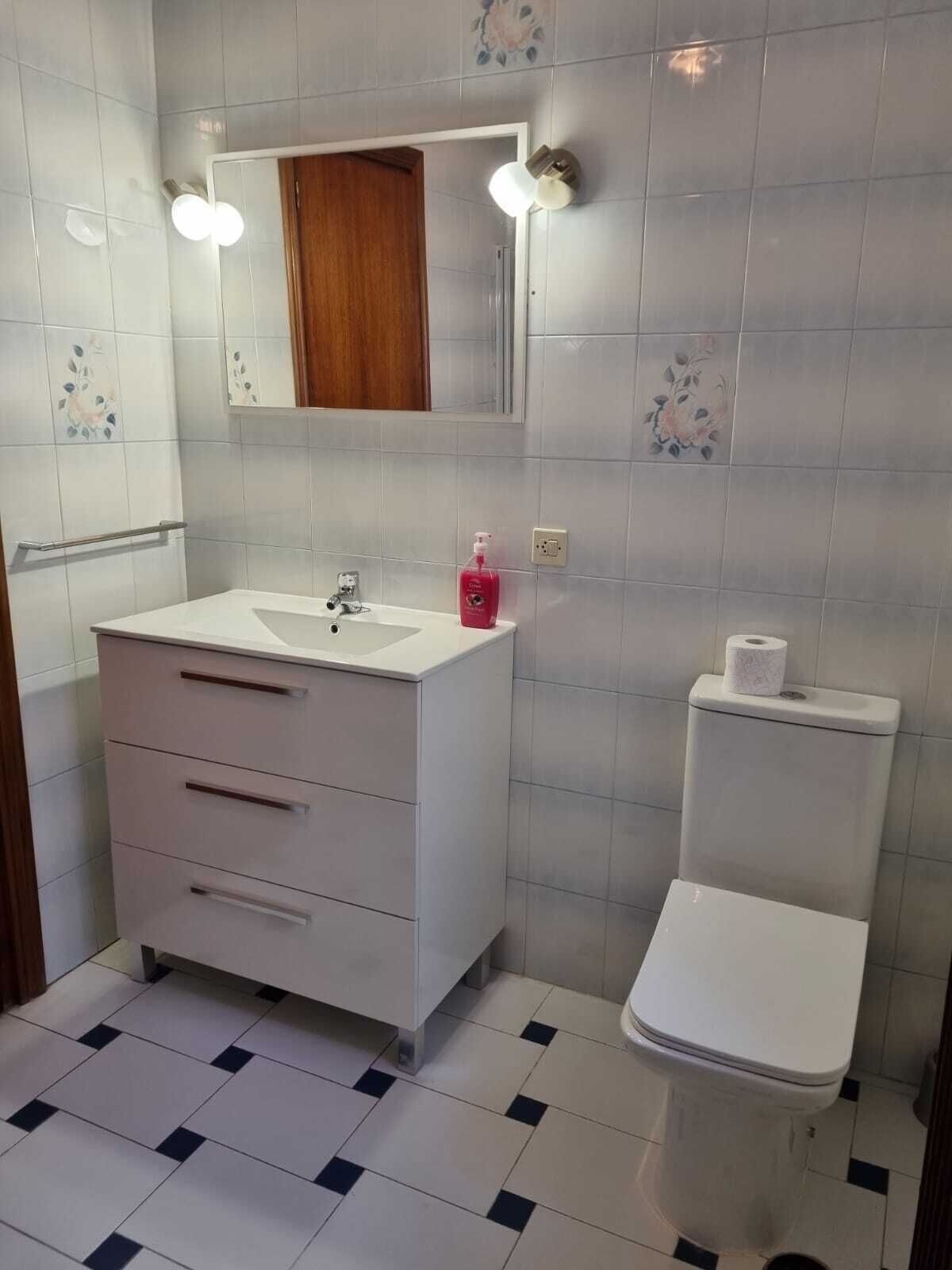 A bathroom with a white sink, mirror, and toilet. There are two wall-mounted lights above the mirror.