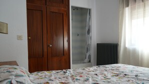 A bedroom with a wooden wardrobe, a shower with a glass door, a radiator, and a bed with a floral bedspread. - Casa Rural Margarita (Peñaranda de Duero)