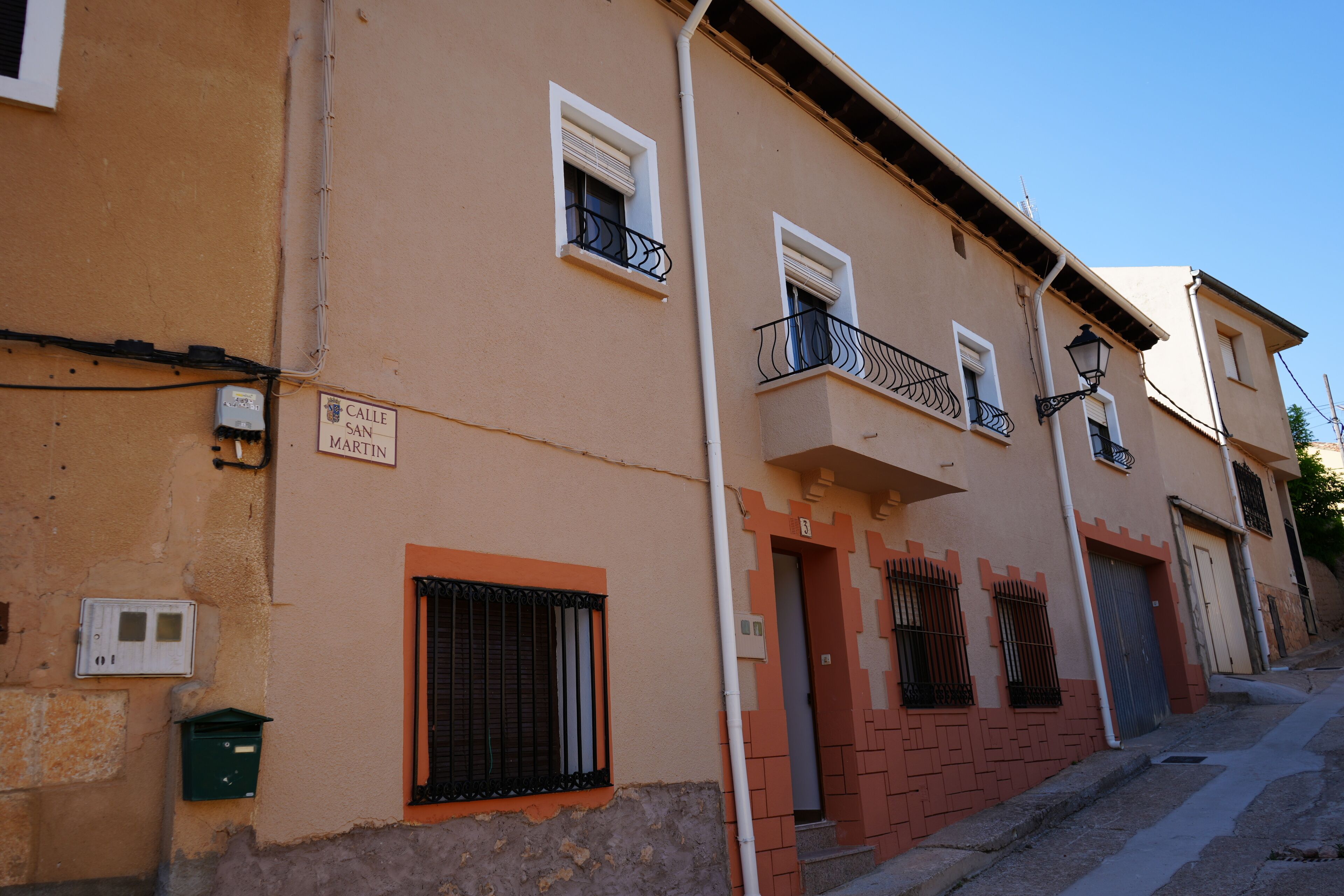 Un immeuble avec une enseigne indiquant « Calle San Martin », doté de balcons avec des garde-corps en métal, d’une porte dont la façade est en briques rouges et d’une petite poubelle verte.