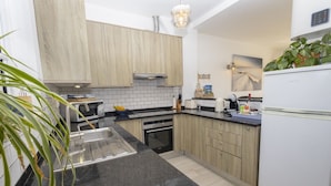 Cocina compacta con armarios de madera, encimera negra, horno empotrado y refrigerador blanco.