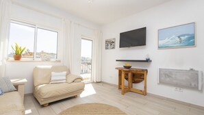 Una sala de estar moderna con un sofá, un televisor, una mesita y vistas de la ciudad a través de amplias ventanas.