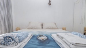 Una cama bien hecha con una colcha azul con motivos marinos, dos almohadas y dos lámparas de noche.