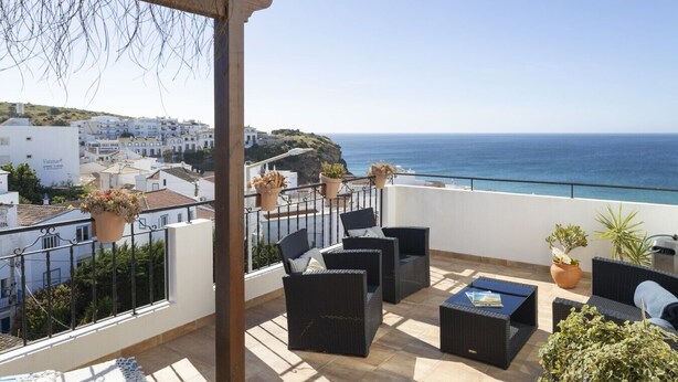 Un balcon aménagé avec du mobilier d’extérieur, des plantes en pot et une vue sur la mer et les bâtiments.