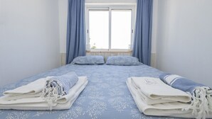 Une chambre à coucher avec un lit, deux oreillers, une fenêtre avec des rideaux et des serviettes pliées.