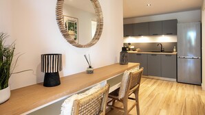 A modern kitchen with grey cabinets, a stainless steel refrigerator, and a wooden dining area with a mirror above the counter. - Appartement vue Mer, Accès Direct Plage D'orient Bay (Orient-Bay)