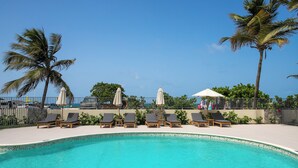 A pool area with lounge chairs and umbrellas, surrounded by palm trees and a clear sky. - Appartement vue Mer, Accès Direct Plage D'orient Bay (Orient-Bay)