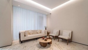 A modern living room with a sofa, two chairs, a coffee table, and a large window with curtains.