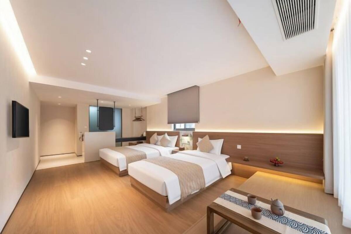 A hotel room with two beds, a small table, a mirror, and a wall-mounted TV.