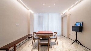 Una sala de conferències amb taula de fusta, cadires, una banca, projector i finestra amb cortines.