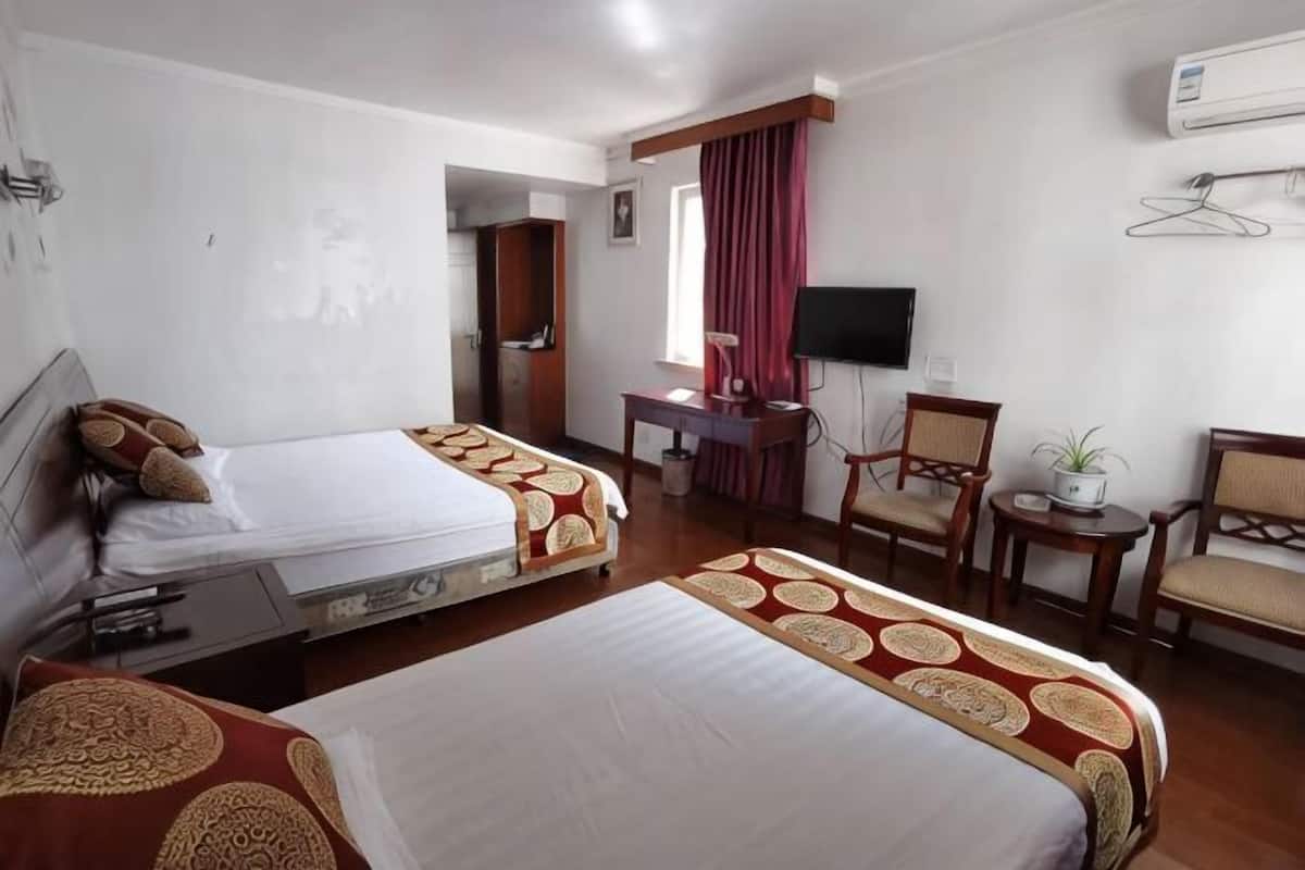 Habitación de hotel con dos camas, un escritorio, una silla, un televisor y un equipo de aire acondicionado.