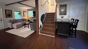 Un salon moderne avec un escalier menant à une salle à manger. Le salon est équipé d’un canapé, d’une table basse et d’un téléviseur. La salle à manger comprend une table et des chaises.
