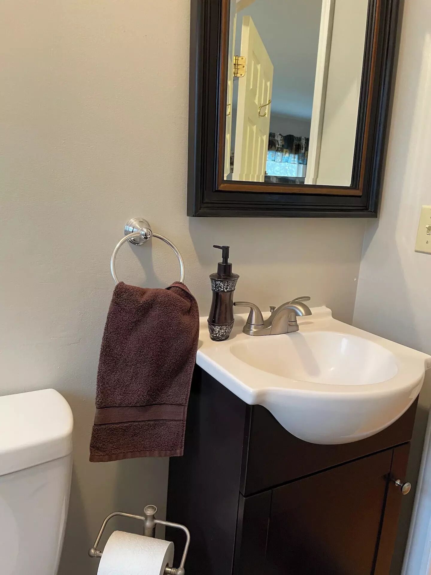 A bathroom with a white sink, dark cabinet, and a towel hanging on a metal holder.