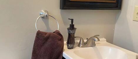 A bathroom with a white sink, dark cabinet, and a towel hanging on a metal holder.
