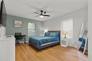 Une chambre à coucher avec un lit, un bureau, une chaise et un ventilateur de plafond.