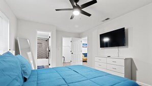 A bedroom with a bed, a ceiling fan, a TV, and a dresser.