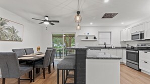 A modern kitchen with white cabinets, a central island, and a dining area with grey chairs and a table.