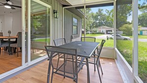 A covered patio with a table and chairs, large sliding glass doors, and a view of a residential street.