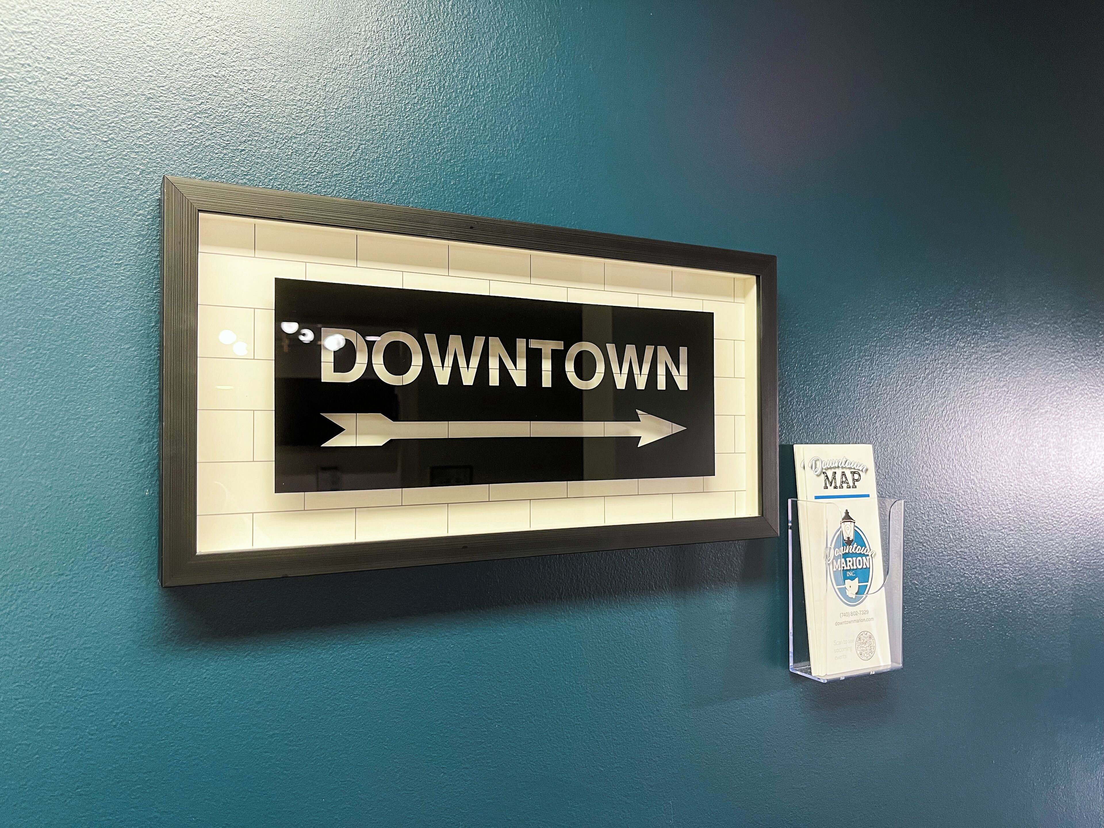 A framed sign with "DOWNTOWN" and an arrow pointing right, mounted on a teal wall.