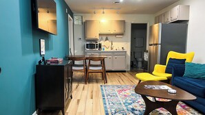 Una cuina moderna amb microones, fogó i nevera. Hi ha una taula de menjador amb caires i un sofà a la zona de sala d'estar.