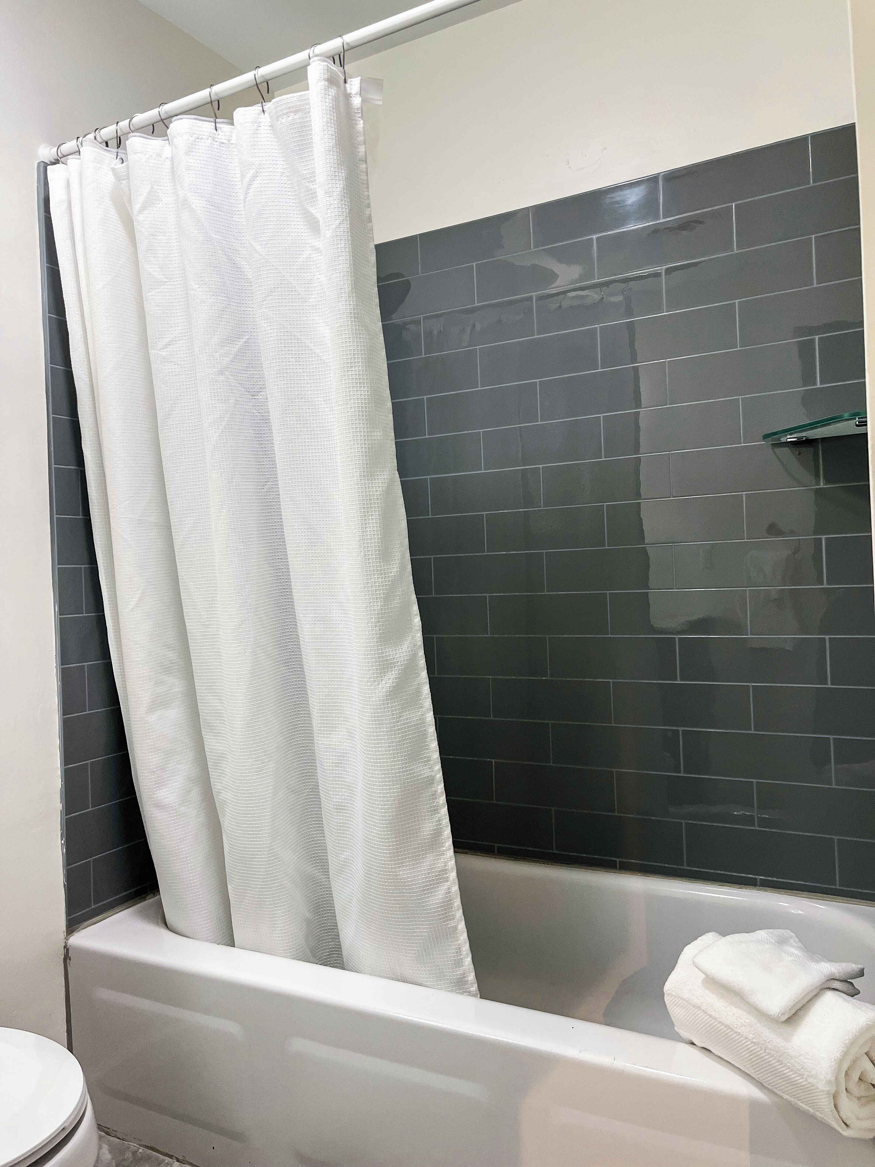 A bathroom with a white bathtub, a white shower curtain, and dark tiled walls.