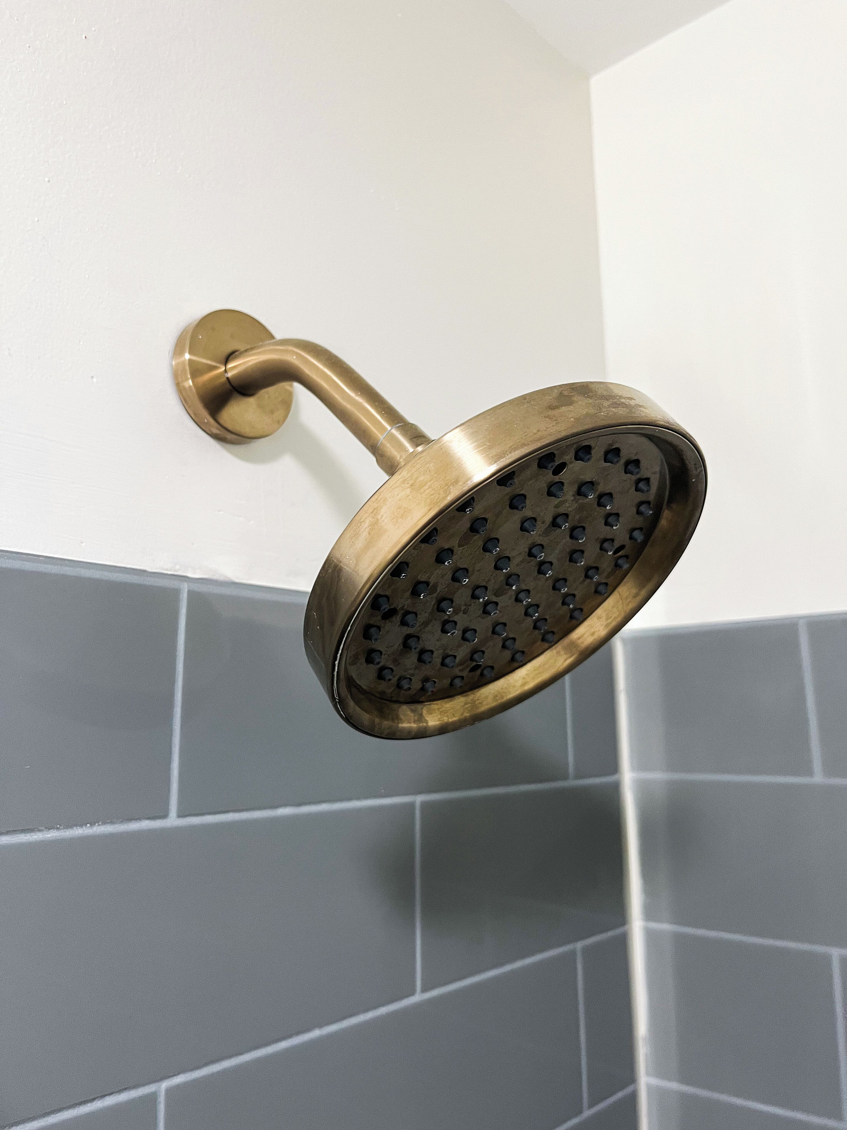 A brass showerhead mounted on a wall with grey tiles.