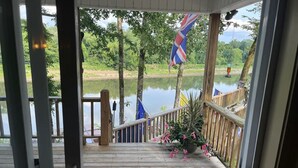 Een houten terras met een hekwerk dat uitkijkt over kalm water, omringd door groen.