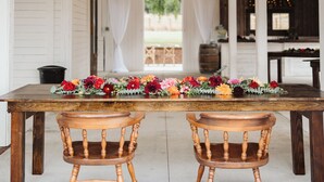 Un área de comedor cubierta con una mesa de madera y dos sillas, decorada con flores y luces de cadena.