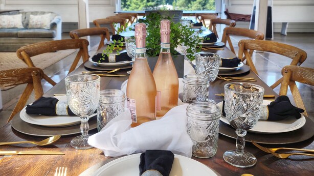 Una mesa de comedor dispuesta para una comida, con dos botellas de champán, copas de cristal y sillas de madera.