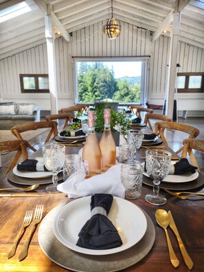 Une table à manger dressée pour un repas, avec deux bouteilles de champagne, de la verrerie en cristal et des chaises en bois.