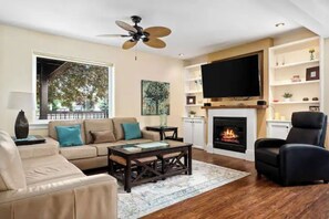 Un salon comprenant un canapé, une table basse, un téléviseur, une cheminée et un ventilateur de plafond.