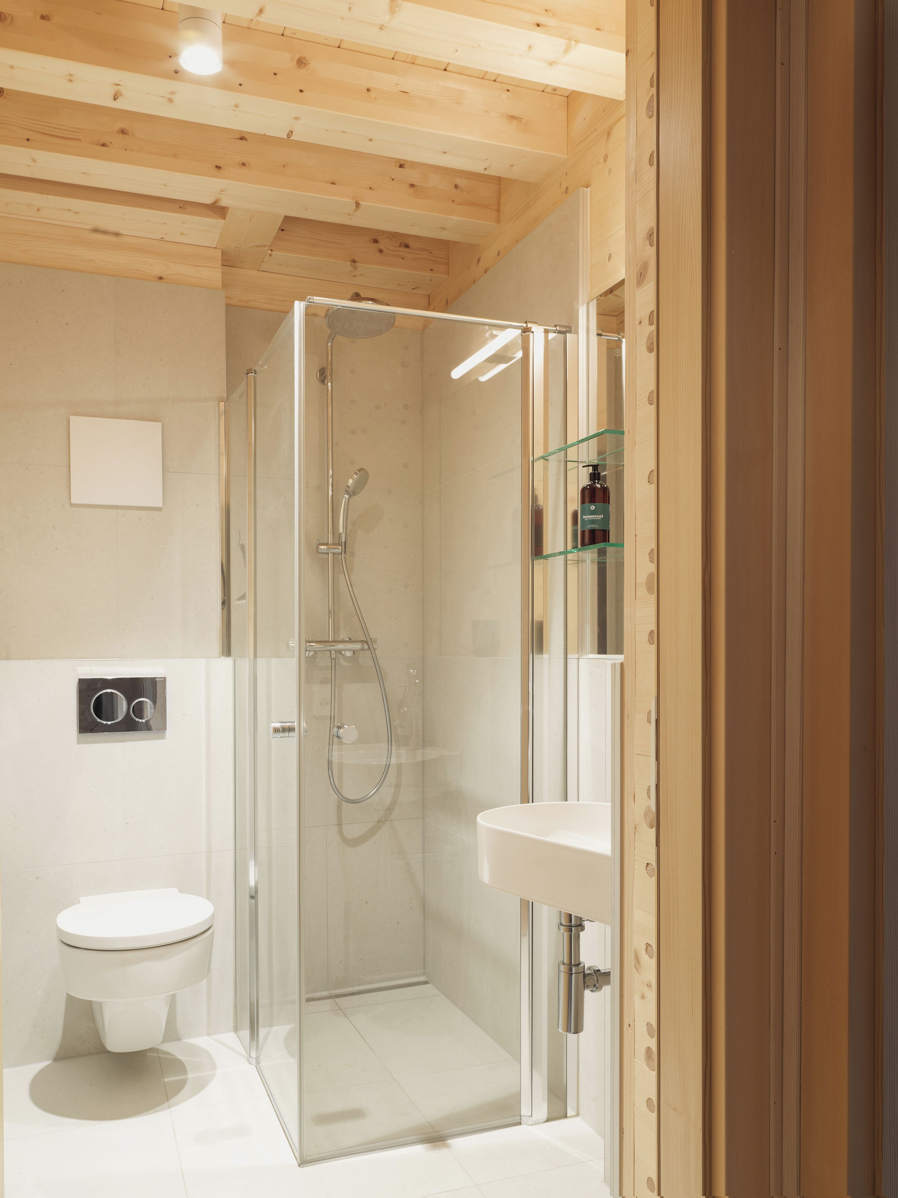 A modern bathroom with a glass-enclosed shower, a white toilet, and a glass shelf with toiletries.