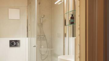 A modern bathroom with a glass-enclosed shower, a white toilet, and a glass shelf with toiletries.