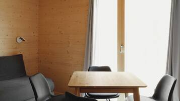 A room with a wooden ceiling, a large window with curtains, a table, and four chairs.