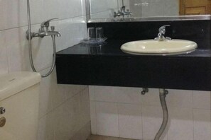 Un baño con un lavamanos blanco, encimera negra y ducha.