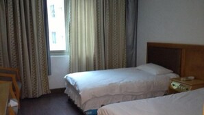 A hotel room with two single beds, a wooden headboard, a bedside table with a lamp, and a window with curtains. - Red Moon Inn (Yueqing)