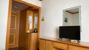 A room with a wooden wardrobe, a television on a wooden stand, and a mirror on the wall. - Red Moon Inn (Yueqing)
