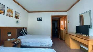 A hotel room with two beds, a wooden desk with a television, and a small table with a lamp.