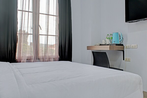 A hotel room with a bed, a desk with a coffee maker, and a TV mounted on the wall. - Capital O 92583 Raja Soeta Hostel Syariah (Bandar Lampung)